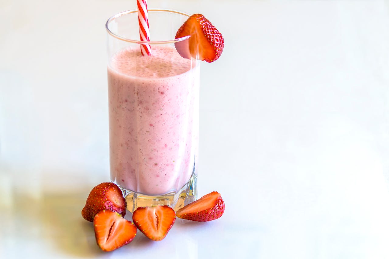 Delicious strawberry smoothie in a glass with fresh strawberries and a striped straw on a light background.