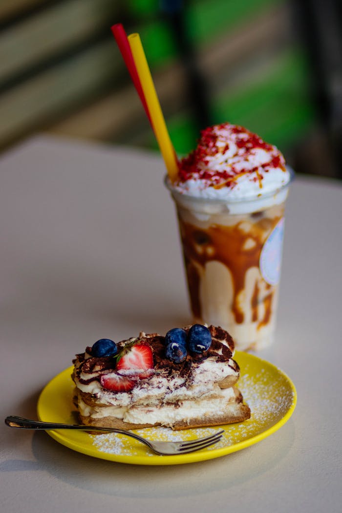 A tempting tiramisu slice with berries and whipped cream milkshake on a table.