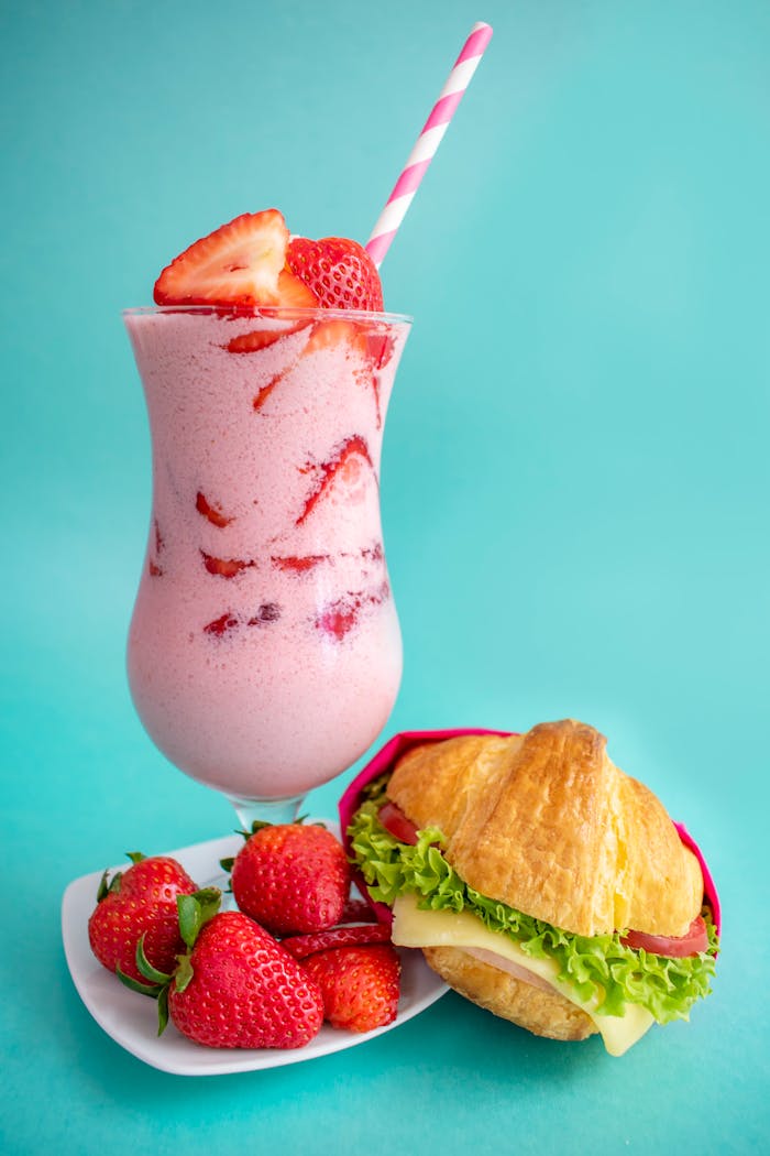 Delicious strawberry milkshake and sandwich served on a colorful background.