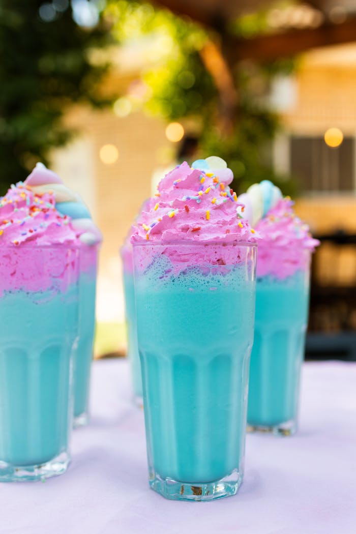 services-01 Colorful unicorn-themed milkshakes with bright pink and blue whipped cream in tall glasses.
