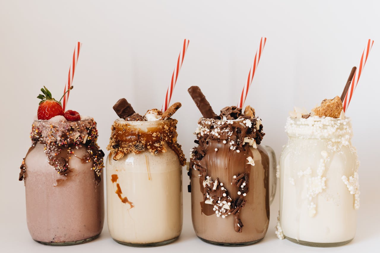 Close-up of four assorted milkshakes with various toppings in glass jars.